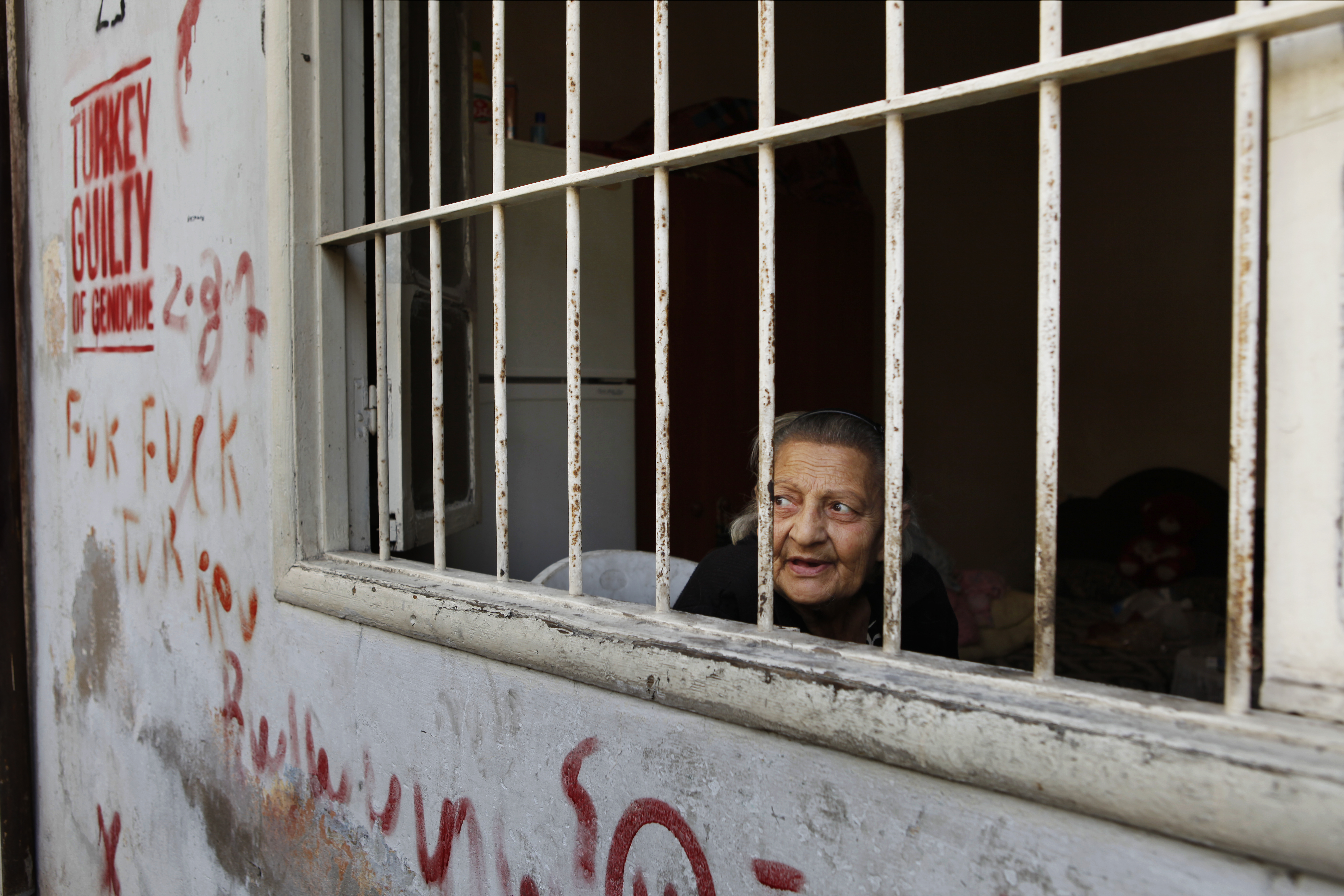 November 4, 2015 Bourj Hammoud, Beirut, Lebanon Imo Vik watches the day go by from her bedroom window in a back alley in central Bourj Hammoud. On the wall beside her, anti-Turkish graffiti keeps the memory of the Armenian genocide fresh in people's minds. Originally from Aleppo, her family moved to Lebanon from Syrian nearly 50 years ago. Today Bourj Hammoud's role as a haven for Syrian-Armenians persists, as some have fled the war in Syria for the relative familiarity and safety of the neighborhood. Imo Vik's docile daily life is reflective of an Armenian demographic reality in Bourj Hammoud in which many young Armenians are leaving the neighbourhood in search of better conditions elsewhere. Those that remain are predominantly elderly inhabitants.