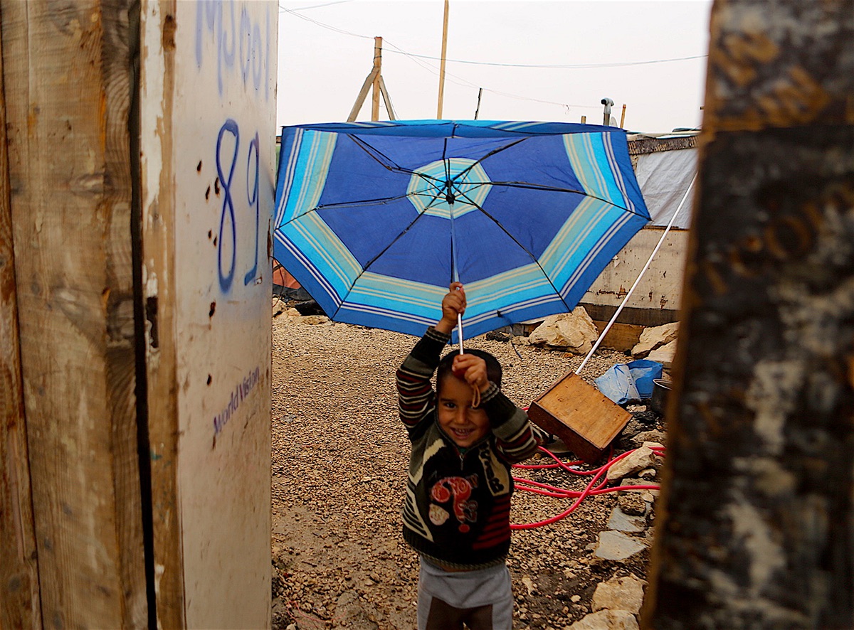 A Syrian boy plays with a broken umbrella outside his tent in the Jaraheyah refugee camp. This photo was taken in Bekaa in Lebanon on Oct. 25, 2015. (Artino)