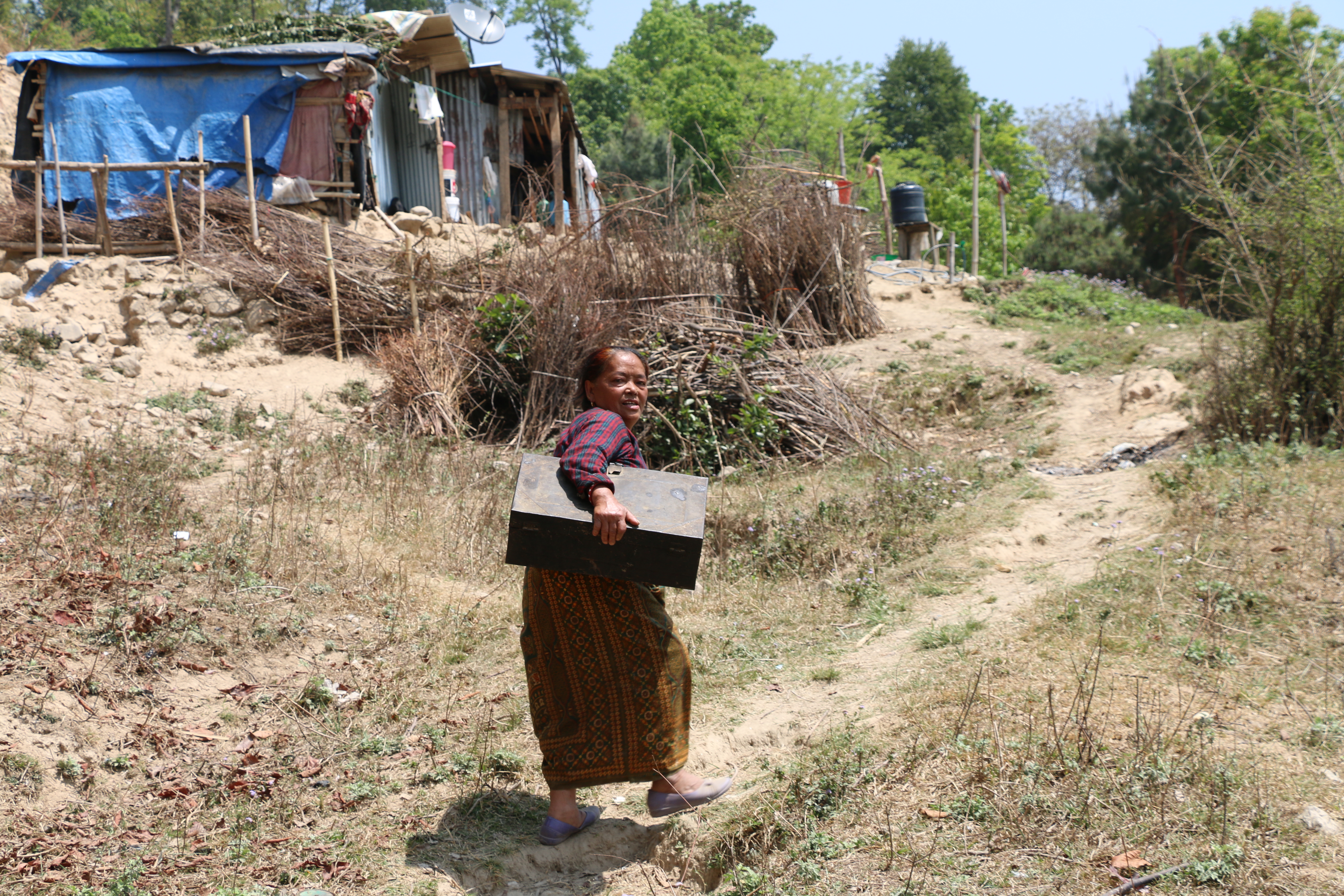 Tamang climbs the hill up to her tin shack holding a box containing a few possessions she retrieved after the earthquake. (Sonia Narang)